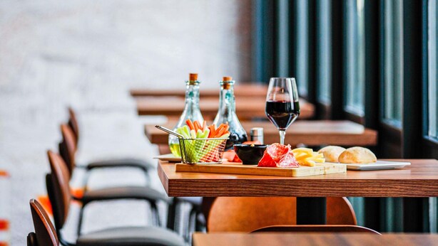A restaurant table with a bottle of wine, a glass of wine, a basket of snacks, and a bottle of water.