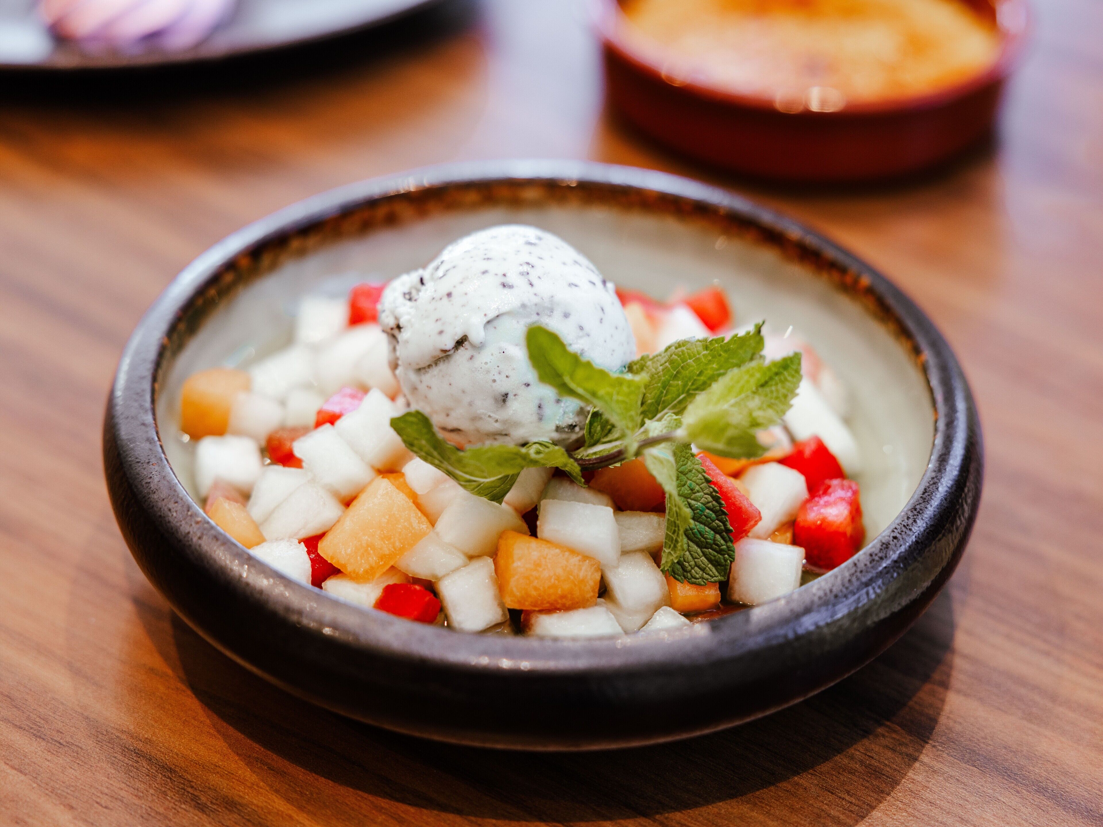 Un postre en un tazón con trozos de fruta y hojas de menta.