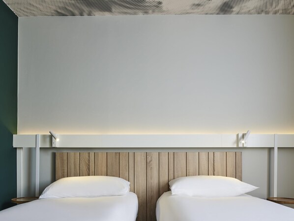 A modern hotel room with two beds, wooden headboard, and a ceiling with a perforated design. - ibis Luxembourg Aéroport (Niederanven)