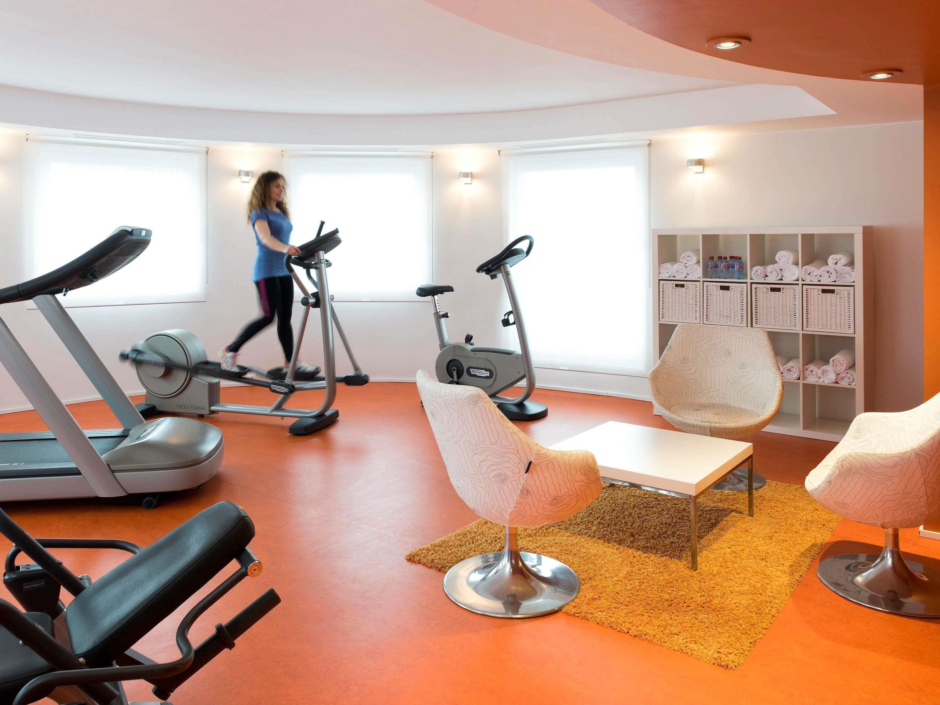Un gimnasio con equipamiento de ejercicio, una cinta de correr y una persona caminando.