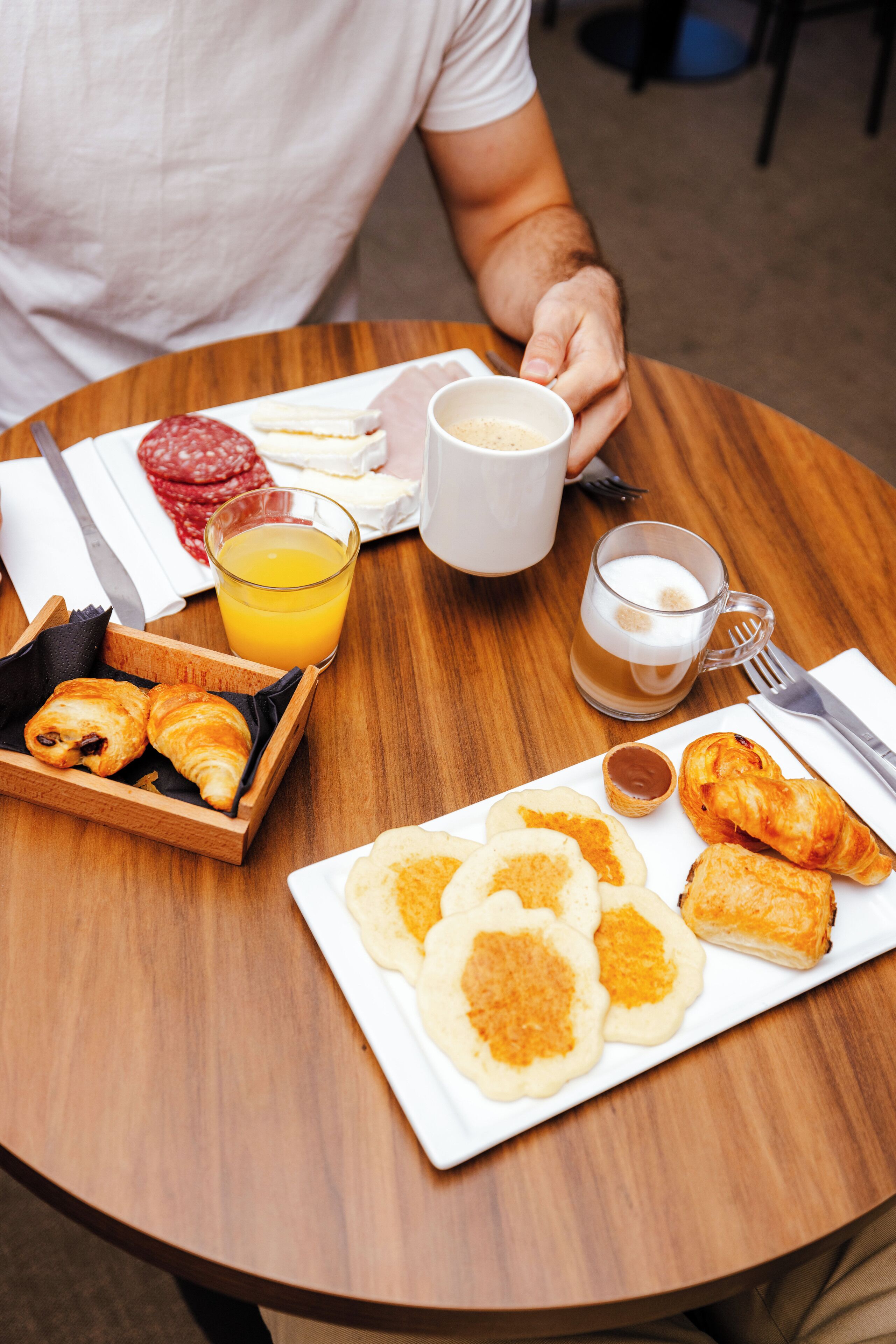 Une table en bois sur laquelle sont disposés des aliments pour le petit-déjeuner, notamment des croissants, des viennoiseries et un verre de jus d’orange.