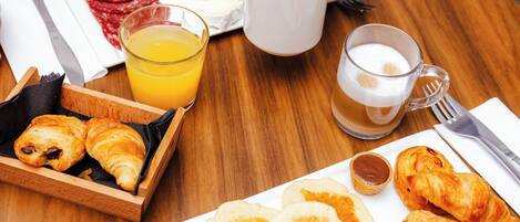 Une table en bois sur laquelle sont disposés des aliments pour le petit-déjeuner, notamment des croissants, des viennoiseries et un verre de jus d’orange.