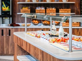 Mostrador de buffet con diversos alimentos y bebidas, incluyendo yogur, fruta y una botella de agua.