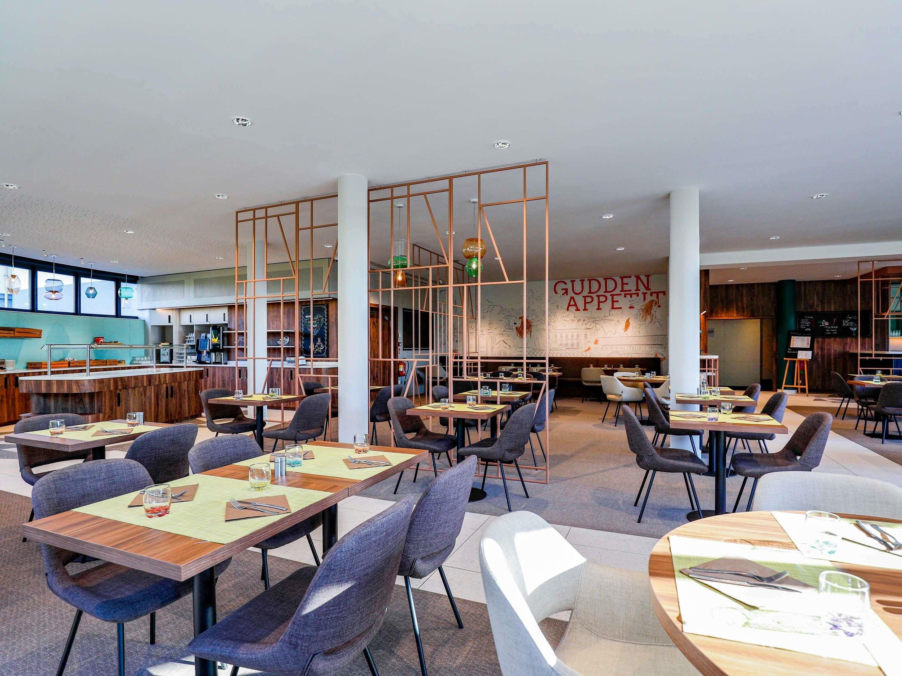 Ein modernes Restaurant mit verschiedenen Essbereichen, einer Bar und einer Wand mit Tafelaushang.