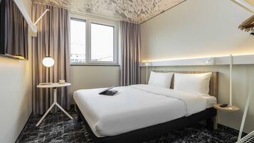 Une chambre d’hôtel avec un lit, un bureau, une lampe et une fenêtre.