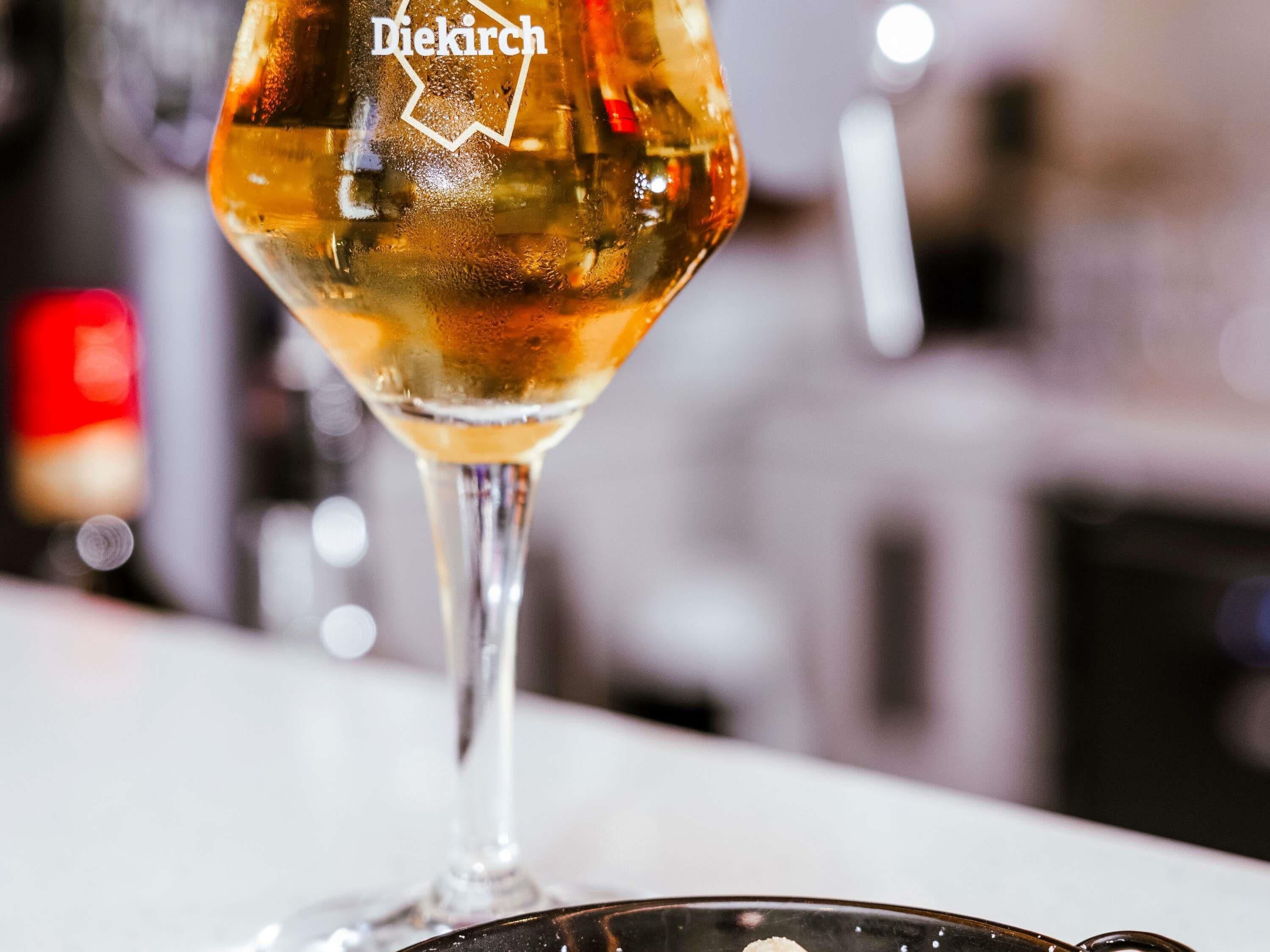 Een glas wijn met een etiket waarop 'Diekirch' staat, op een barkruk.