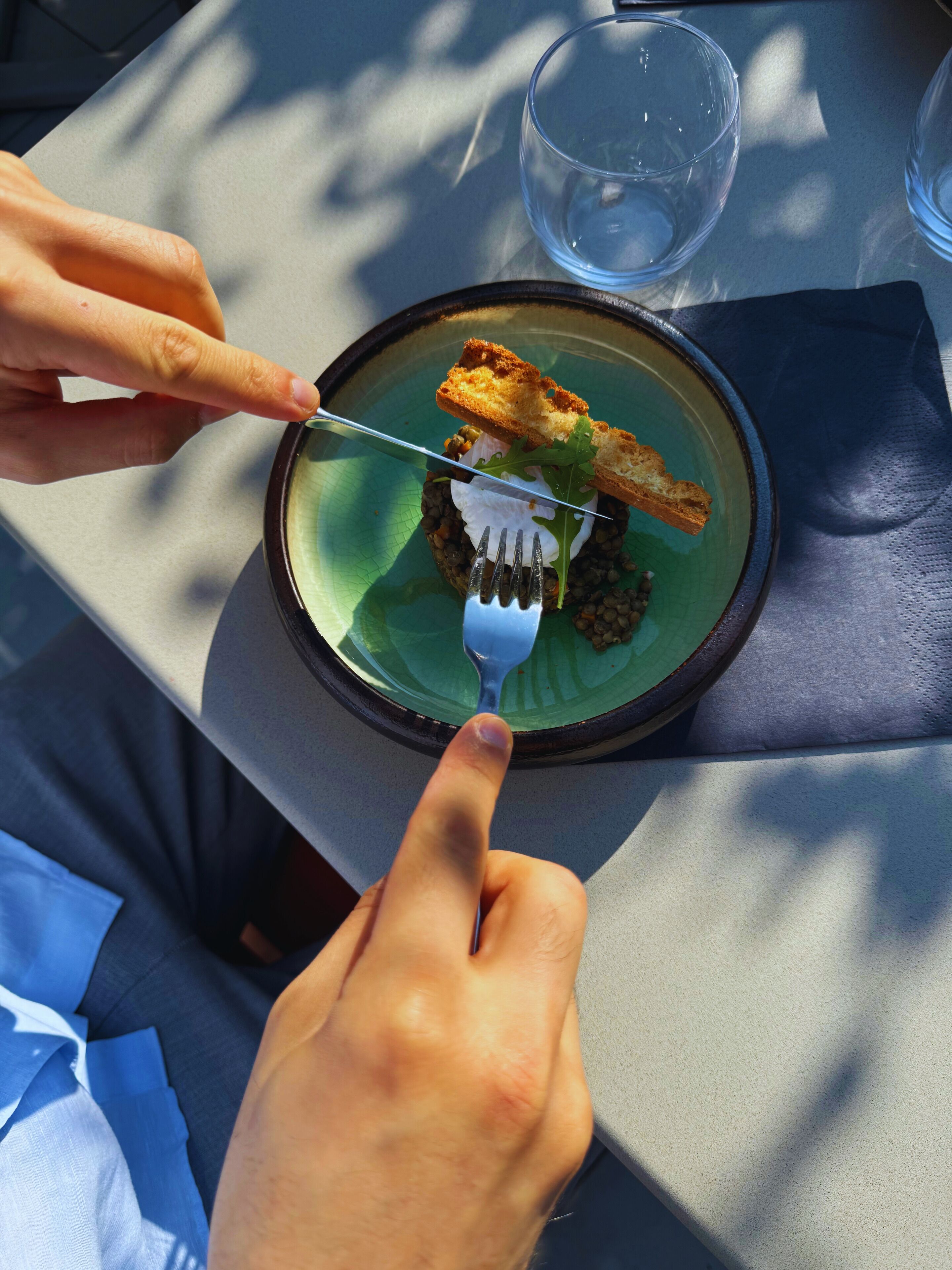 A person dining at a table with a plate of food, a fork, and a glass of water.