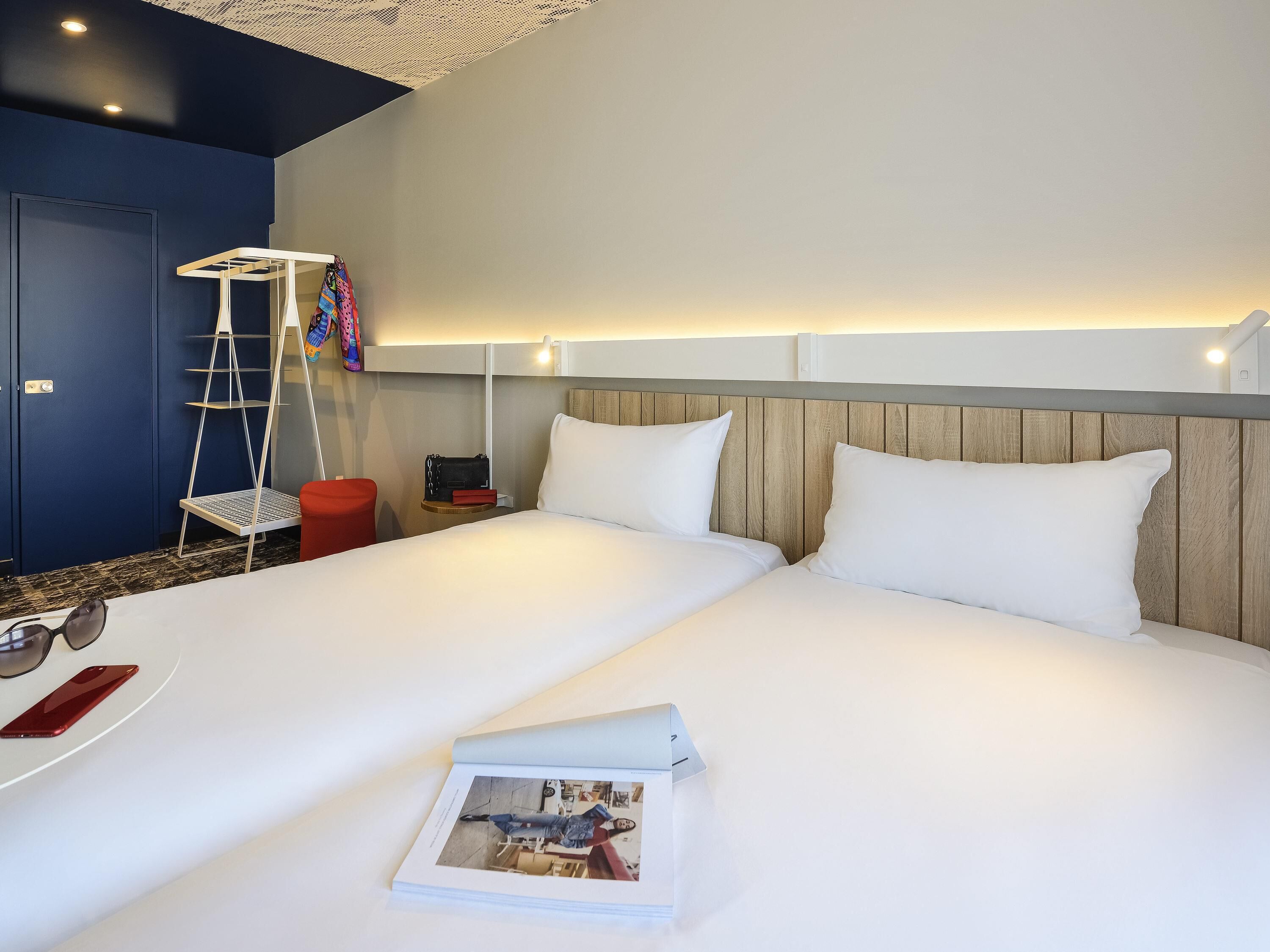 Ein Hotelzimmer mit einem großen Bett, einem Nachttisch, einem roten Sessel, einer Hartsreppe und einem Wandregal.