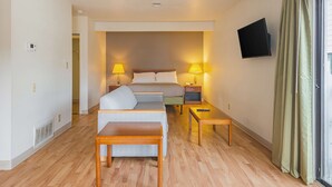 Ein Hotelzimmer mit Bett, zwei Nachttischen, einer Couch, einer Holzbank, einem Fernseher und einem Fenster mit Vorhängen.