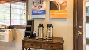 Ein Hotelzimmer mit Fenster, einer Wand-Klimaanlage, einer Kaffeestation mit zwei elektrischen Wasserkochern und zwei Postern, die Dienstleistungen bewerben.