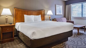 A hotel room with a large bed, two bedside tables with lamps, a small armchair, and a window with a view.