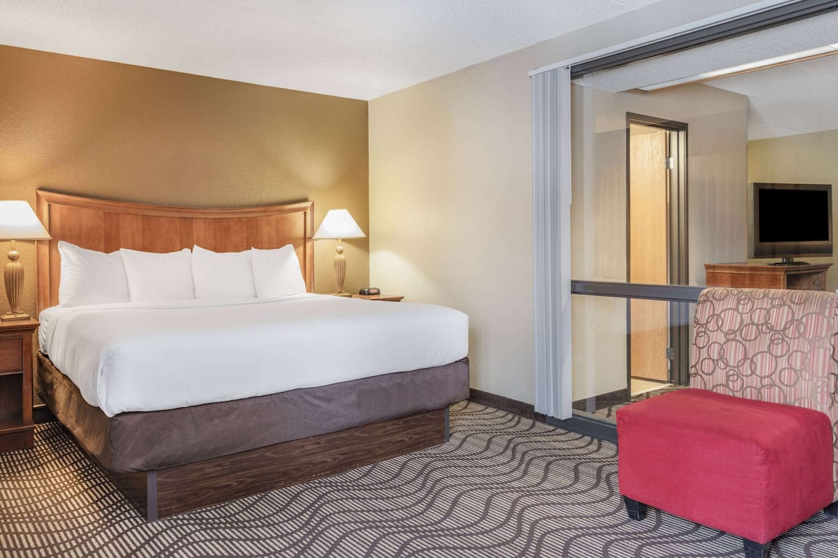 Une chambre d’hôtel avec un grand lit, deux lampes de chevet, un fauteuil rouge et un téléviseur posé sur un meuble en bois.