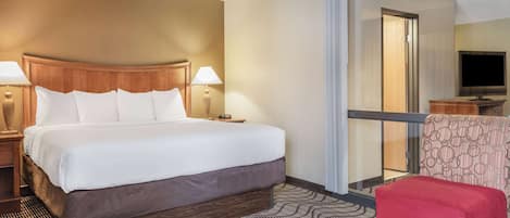 Habitación de hotel con una cama grande, dos lámparas de noche, una silla roja y un televisor sobre un soporte de madera.