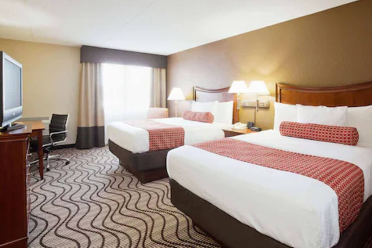 Une chambre d’hôtel avec deux lits, un bureau avec une chaise, une télévision et une moquette à motifs.