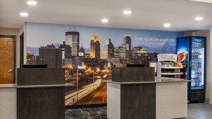 A hotel reception area with a cityscape mural, a Pepsi refrigerator, and a reception desk.