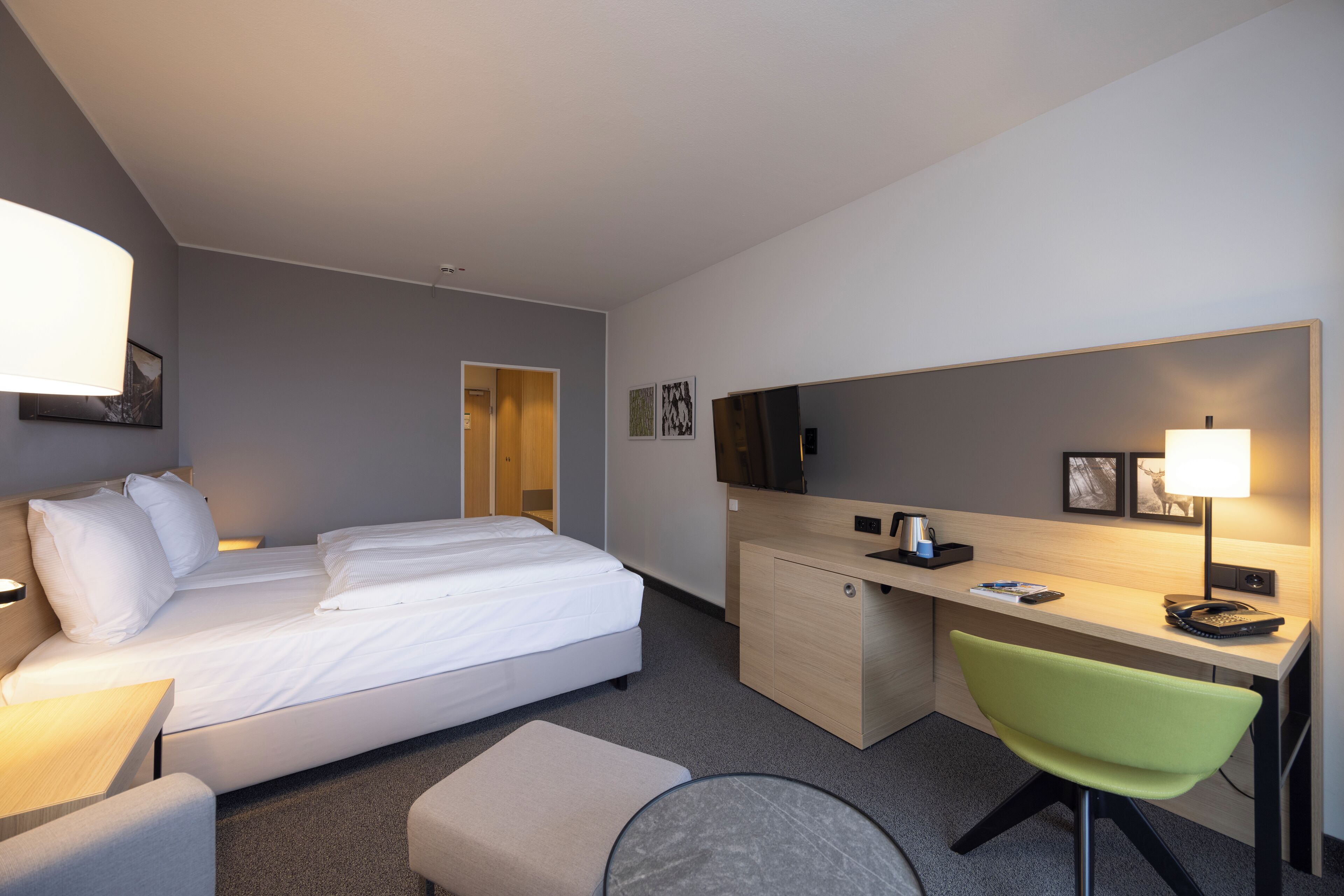 A hotel room with a bed, desk, chair, and a television.