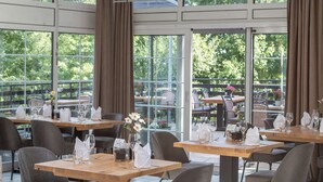 An indoor dining area with tables set for service, large windows, and a view of the outdoors.