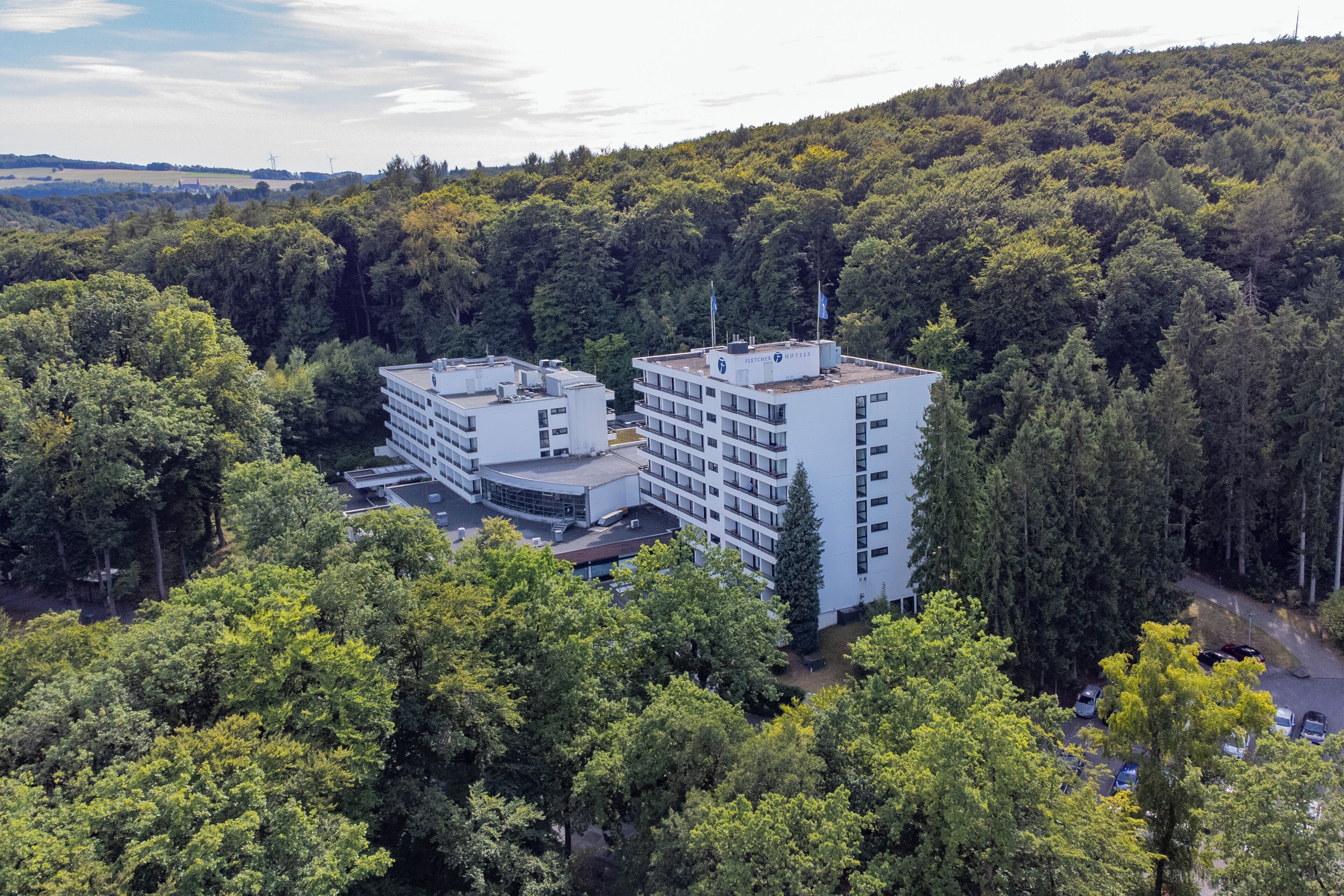 A multi-story hotel with a flat roof, surrounded by dense forest.