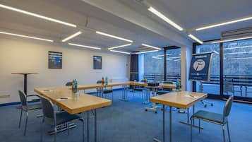 Sala de conferências com mesas, cadeiras, janelas amplas e um banner.
