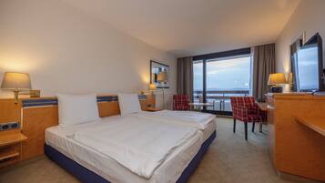 A hotel room with a large bed, a desk, a chair, and a view of the city.