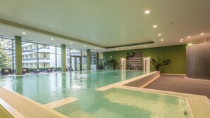 An indoor swimming pool with clear water, surrounded by a green wall and a balcony with multiple levels.