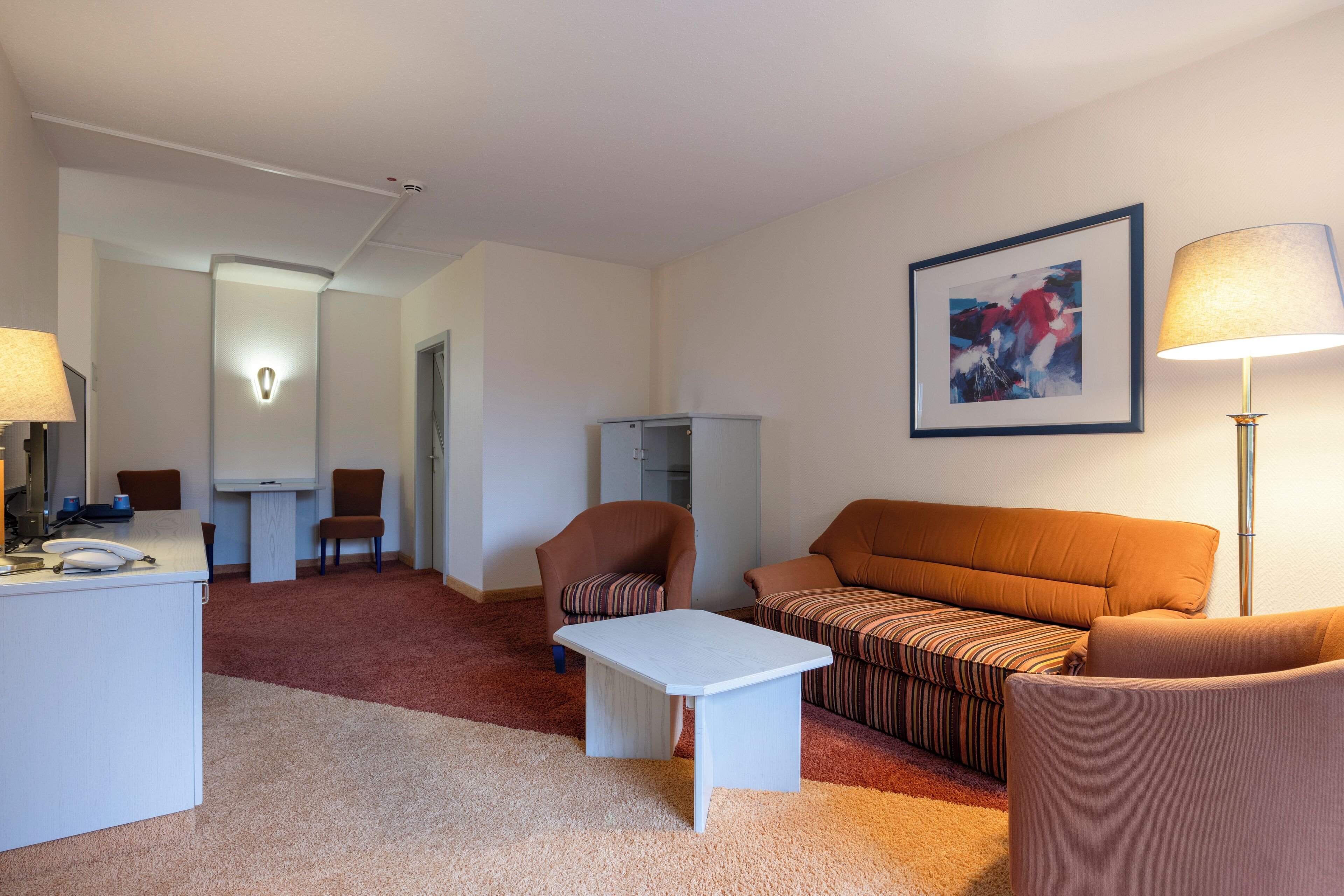 Camera d'albergo con divano, poltrona, scrivania e un quadro appeso al muro.