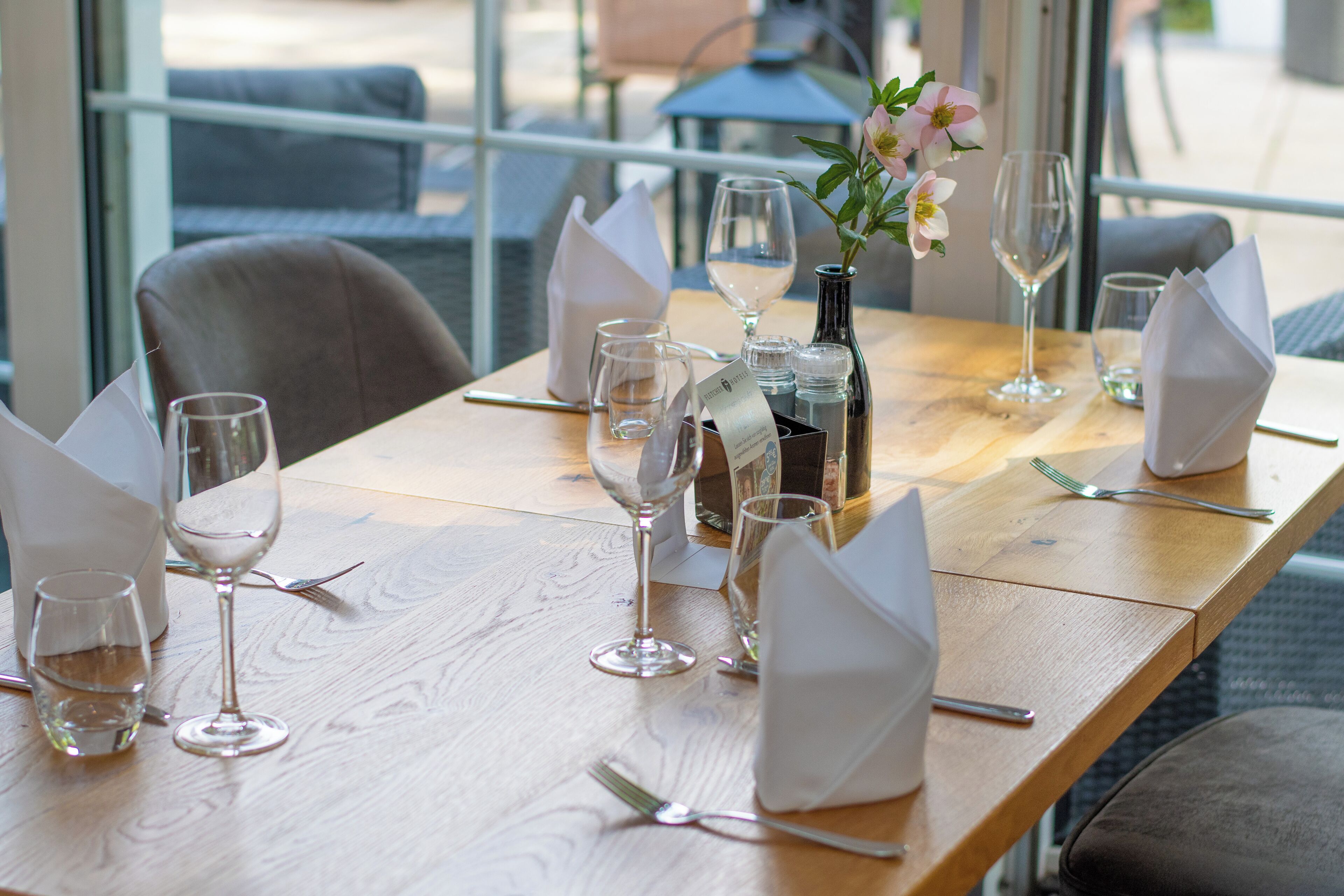 Une table à manger dressée avec des verres à vin, un vase rempli de fleurs et des serviettes soigneusement pliées.