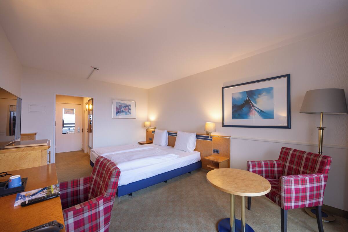 Une chambre d’hôtel avec un lit, un bureau, une chaise, une table et une lampe.