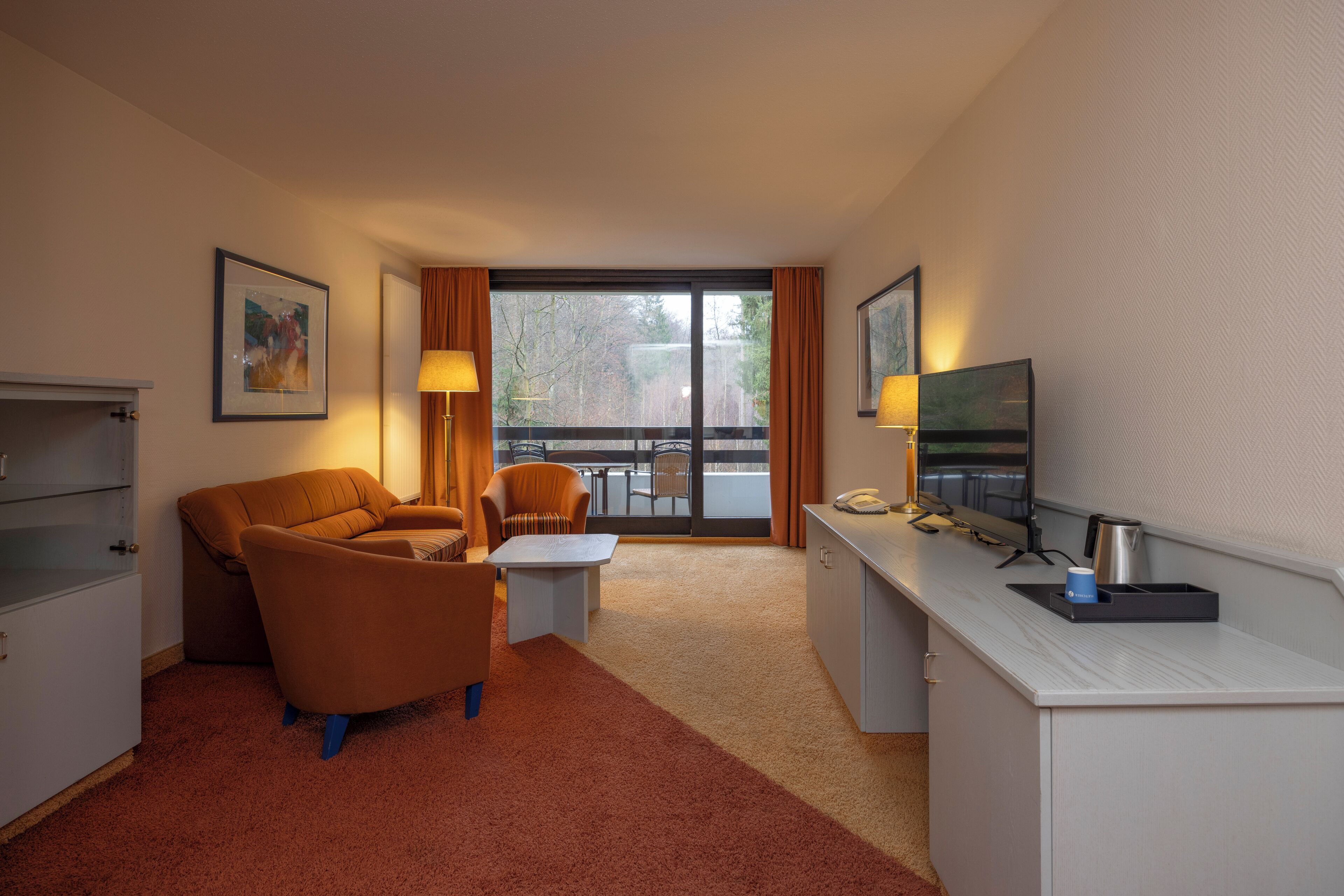 Une chambre d’hôtel équipée d’un canapé, d’un fauteuil, d’une petite table, d’un bureau avec une télévision et offrant une vue sur l’extérieur.