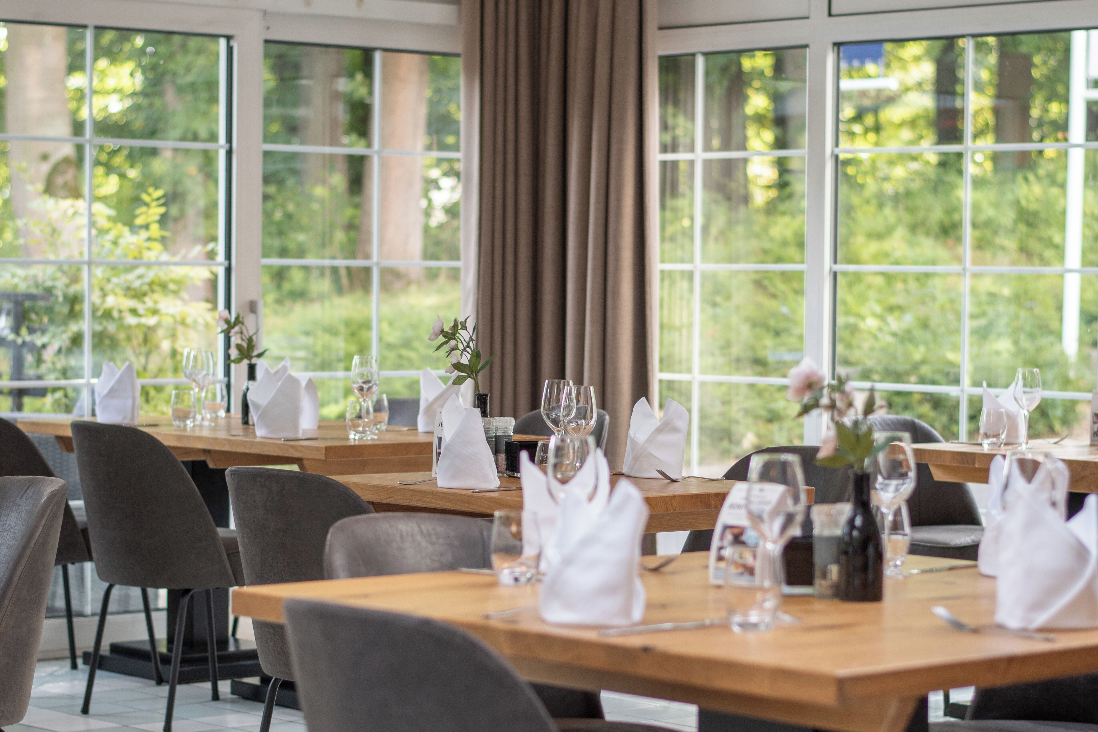 Ein Restaurant mit gedeckten Tischen, großen Fenstern und Blick ins Grüne.