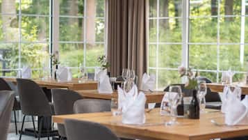 A restaurant with tables set for dining, large windows, and a view of greenery.