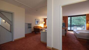Quarto de hotel com cama, escrivaninha, cadeira, sofá e uma grande janela com cortinas.