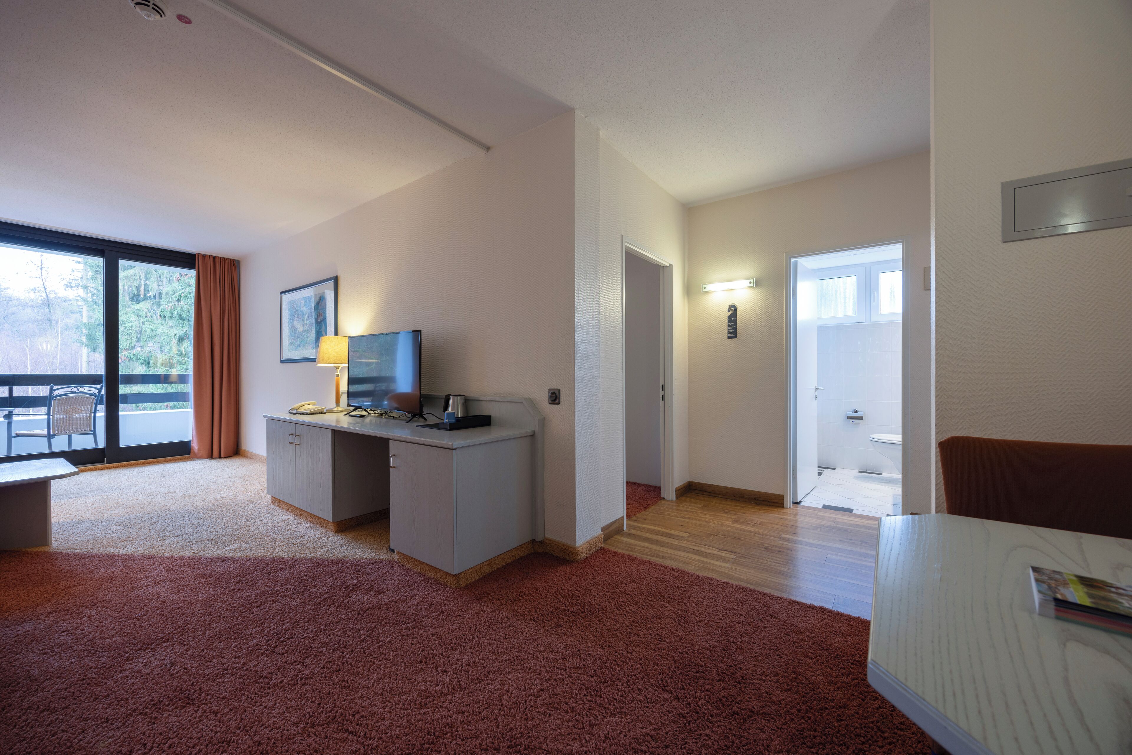 A hotel room with a desk, a chair, a bed, a window, and a door leading to the bathroom.