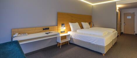A hotel room with a bed, a desk, a chair, and a bedside table.