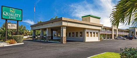 A Quality Inn with a signboard, a parking lot, and a building with a flat roof and a balcony.