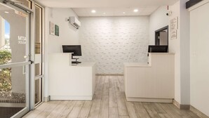 Zona de recepción con pared de ladrillo blanco, dos mostradores de recepción y una puerta de vidrio que da al exterior.