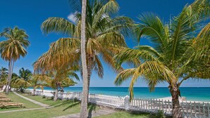 A beachside view with palm trees, a white fence, and a clear blue sky. - Radisson Grenada Beach Resort (St. George's)
