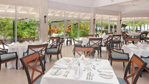A restaurant with tables set for dining, large windows, and indoor plants. - Radisson Grenada Beach Resort (St. George's)