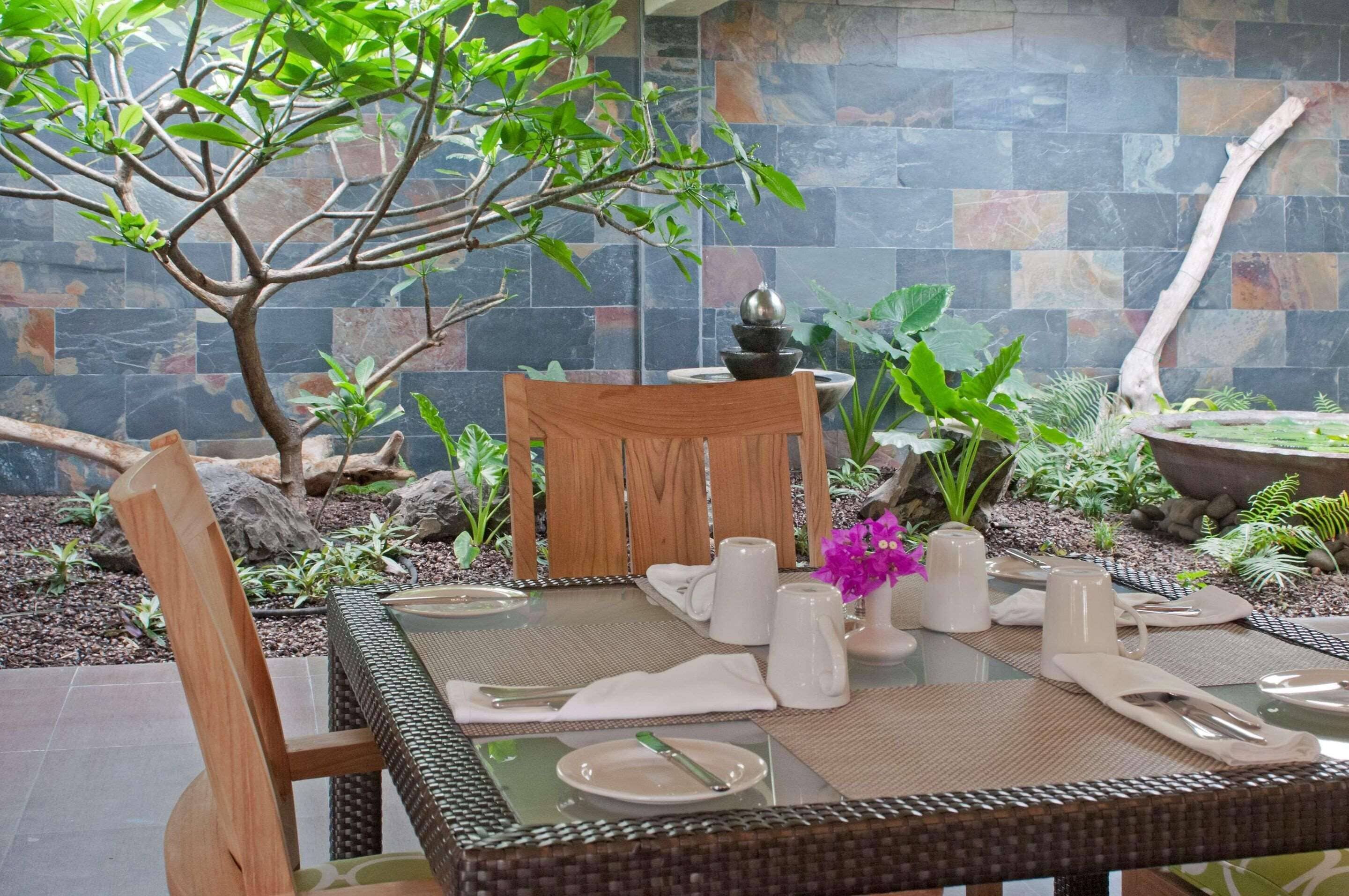 Un comedor con una mesa de vidrio, sillas de madera y un fondo de pared de piedra.