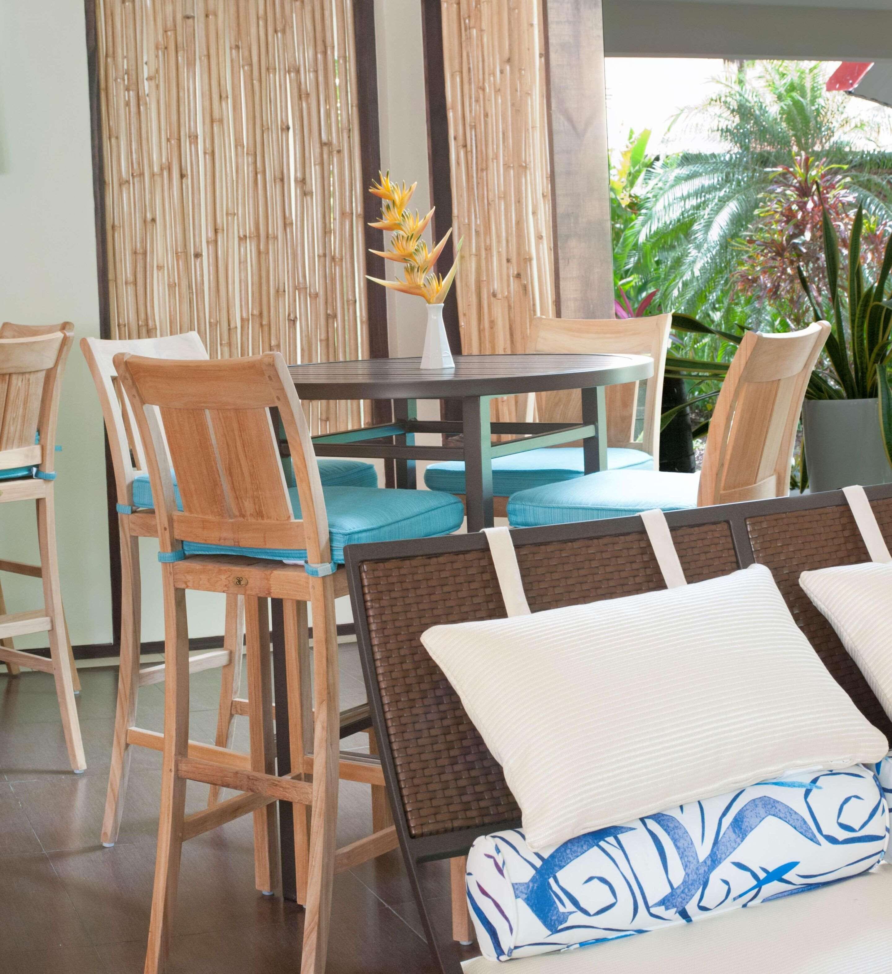 A dining area with wooden chairs and a round table, surrounded by bamboo walls and potted plants.
