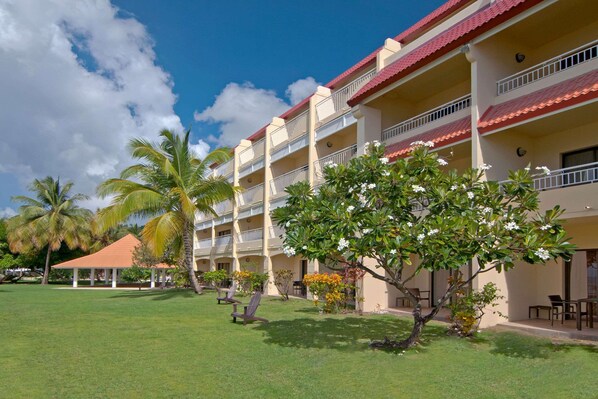 A hotel with multiple balconies, a covered outdoor seating area, and palm trees.