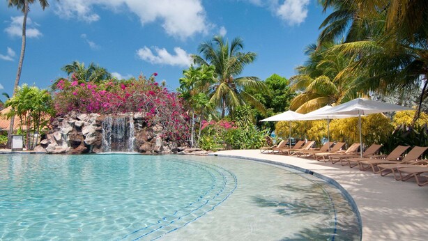 A clear swimming pool with a waterfall feature, surrounded by palm trees and lounge chairs. - Radisson Grenada Beach Resort (St. George's)