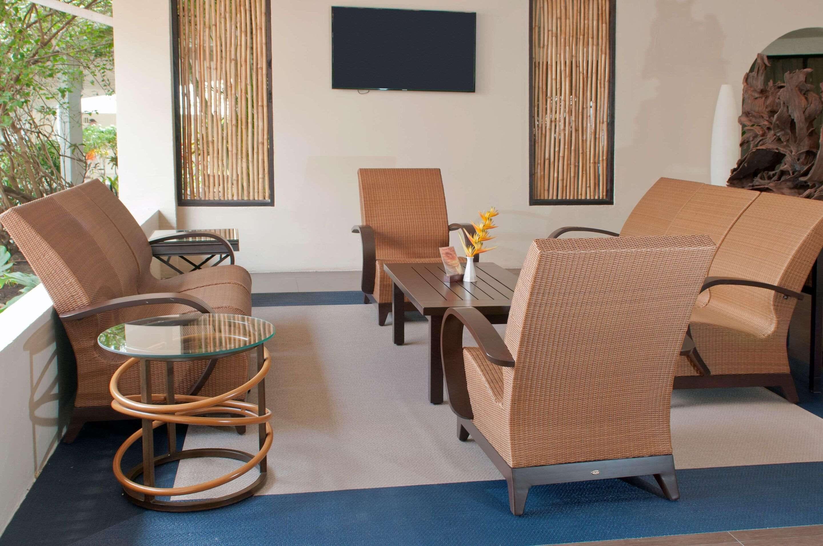 Un espace de détente moderne, avec des meubles en osier, une table en verre et un téléviseur à écran plat fixé au mur.