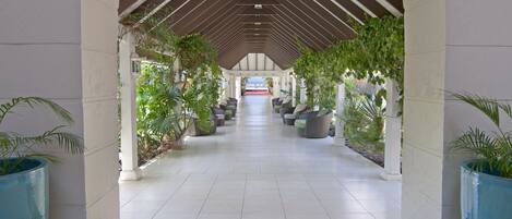 A covered corridor with tiled flooring, columns, and potted plants.