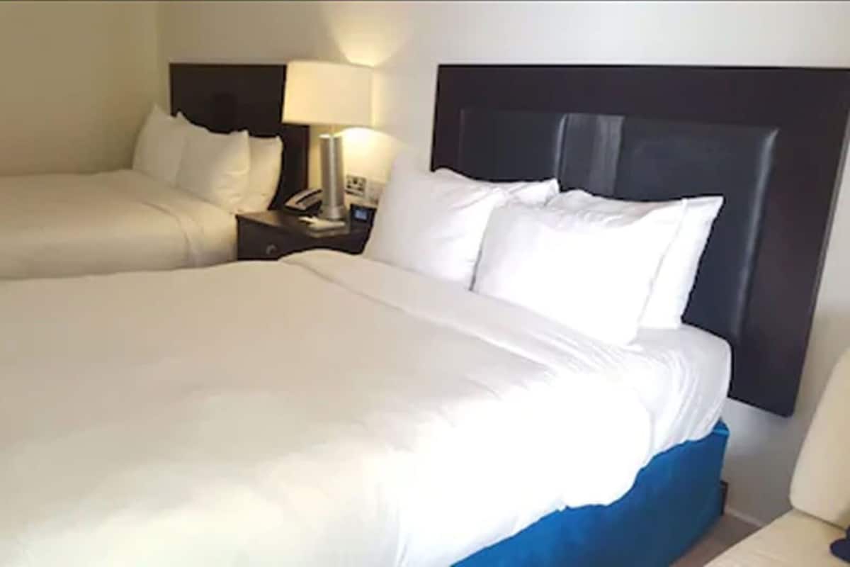 A hotel room with two beds, a nightstand with a lamp, and a headboard.