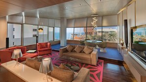 A spacious living area with a modern design, featuring a large sofa, a coffee table, and a dining table with chairs. Large windows offer a view of the cityscape and a building with a distinctive dome structure.