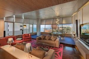 Amplia sala de estar de diseño moderno, con un sofá grande, una mesa de centro y una mesa de comedor con sillas. Ventanales ofrecen vistas al paisaje urbano y un edificio con una estructura de cúpula distintiva.