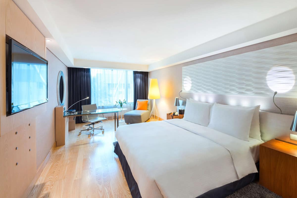 A modern hotel room with a large bed, a desk, a chair, a TV, and a window with curtains.