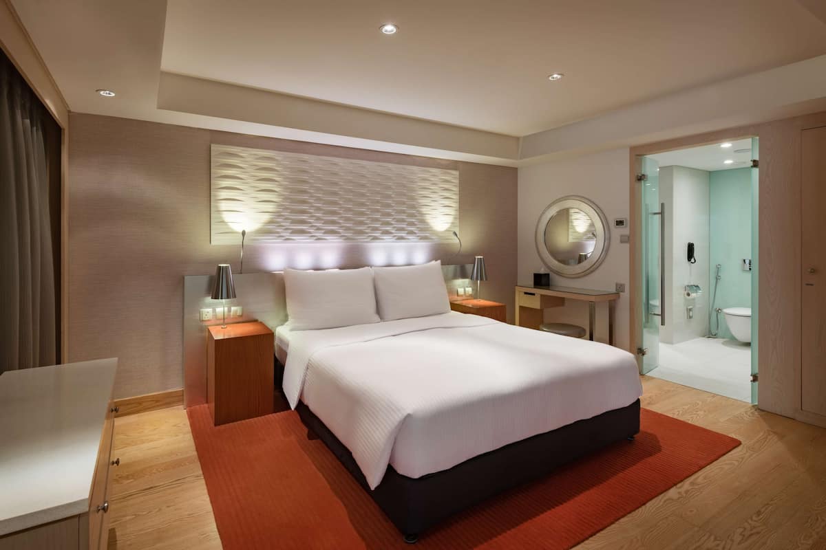 A modern hotel room with a large bed, bedside tables, a mirror, and a bathroom visible through an open door.