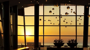 A room with large windows, a view of the sunset, and hanging spherical lights.